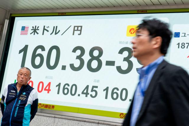 Pedestrians walk past an electronic quotation boards displaying the foreign exchange rate of the Japanese yen against the US dollar along a street in Tokyo on April 30, 2026. (Photo by Kazuhiro NOGI / AFP)