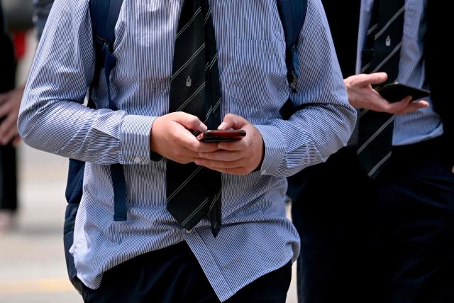 (FILES) A file photo taken on November 28, 2024 shows young people looking at their phones in Melbourne as Australia looks to ban children under 16 from social media. There was "no meaningful shift" away from big tech platforms like TikTok and Instagram in the immediate wake of Australia's world-leading teen social media ban, government documents obtained by AFP show. (Photo by William WEST / AFP)