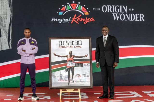 Kenya's President William Ruto (R) poses with Kenyan marathon runner Sabastian Sawe (L) on stage next to a picture of him while crossing the finish line to win the London Marathon after breaking a historic world record, during a congratulatory ceremony at State House in Nairobi, on April 30, 2026. Sabastian Sawe became the first man to run under two hours for a marathon in race conditions thanks to extraordinary talent, a punishing training regime, and the lightest shoes in history. In London on April 26, 2026, the 31-year-old Kenyan achieved one of sport's milestones, ranking alongside Roger Bannister's first sub-four minute mile in 1954. (Photo by Luis TATO / AFP)