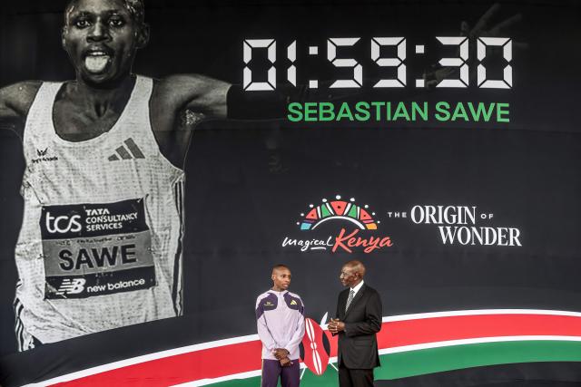 Kenya's President William Ruto (R) congratulates Kenyan marathon runner Sebastian Sawe (L) on stage during a ceremony at State House in Nairobi, on April 30, 2026, after breaking a historic world record at the London Marathon. Sebastian Sawe became the first man to run under two hours for a marathon in race conditions thanks to extraordinary talent, a punishing training regime, and the lightest shoes in history. In London on April 26, 2026, the 31-year-old Kenyan achieved one of sport's milestones, ranking alongside Roger Bannister's first sub-four minute mile in 1954. (Photo by Luis TATO / AFP)