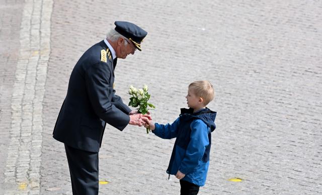 Sweden's King Carl XVI Gustaf is given flowers by a boy during the changing of the guard ceremony to pay tribute to the King at the Outer Courtyard of the Royal Palace in Stockholm, Sweden, on April 30, 2026, during celebrations to mark the 80th birthday of the King. (Photo by Jonathan Nackstrand / AFP)