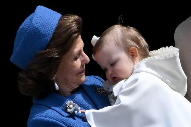 Queen Silvia of Sweden holds Princess Ines Marie Lilian Silvia in her arms, standing on the balcony to watch the changing of the guard as members of the Swedish Armed Forces pay tribute to the King at the Outer Courtyard of the Royal Palace in Stockholm, Sweden, on April 30, 2026, during celebrations to mark the 80th birthday of Sweden's King Carl XVI Gustaf. (Photo by Jonathan Nackstrand / AFP)
