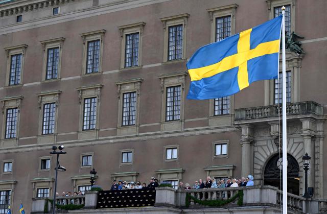 The Swedish flag flutters in the wind as members of the Swedish Royal Family stand on a balcony to watch a flyover performance of members of the Swedish Air Force, at the Royal Palace in Stockholm, Sweden, on April 30, 2026, during celebrations to mark the 80th birthday of Sweden's King Carl XVI Gustaf. (Photo by Jonathan Nackstrand / AFP)