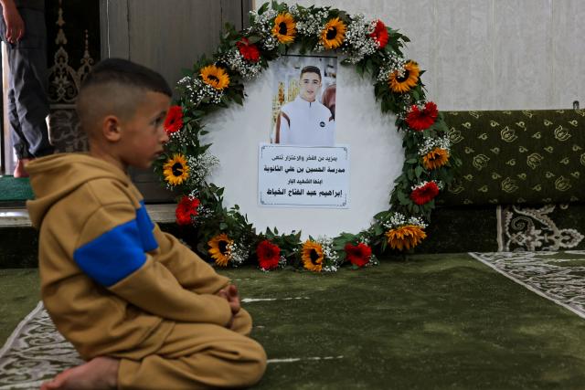 A boy sits beside a wreath bearing a portrait of 16-year-old Palestinian Ibraheem Khayyat, who was killed in an Israeli raid, during his funeral in the occupied West Bank city of Hebron on April 30, 2026. (Photo by HAZEM BADER / AFP)