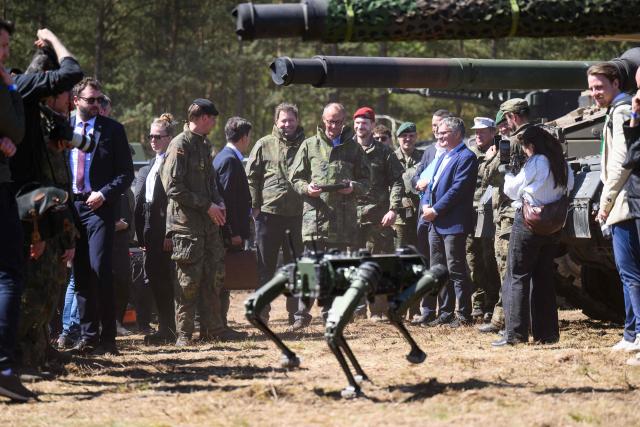 German Chancellor Friedrich Merz (C), operates a robot dog with a remote control during his visit to the German army barracks in Munster, northern Germany, on April 30, 2026. (Photo by DANIEL REINHARDT / AFP)