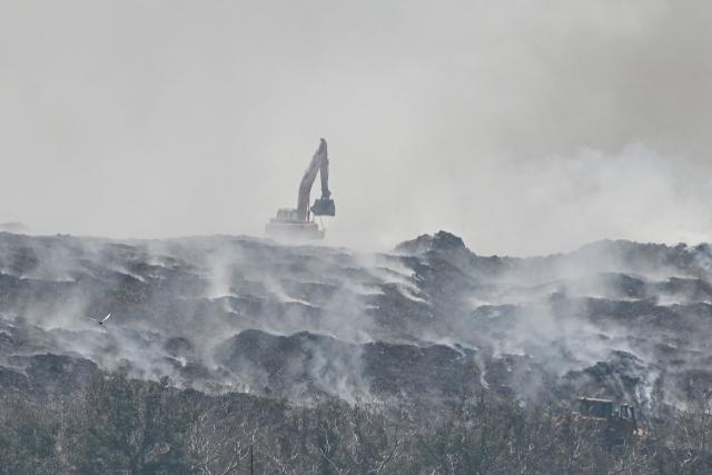Heavy equipment work on a burning landfill in the nearby Navotas City, as seen from a boat along the coast of Obando town, Bulacan province, on April 30, 2026. The fire at Metro Manila's Navotas landfill is largely invisible to the naked eye, combusting as deep as 15 metres (50 feet) below the surface and releasing a toxic brew of methane as well as carbon dioxide. (Photo by Ted ALJIBE / AFP) / To go with "PHILIPPINES-FIRE-WASTE-ENVIRONMENT-POLLUTION, REPORTAGE" BY PAM CASTRO