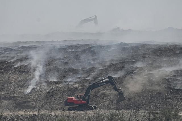 Heavy equipment work on a burning landfill in the nearby Navotas City, as seen from a boat along the coast of Obando town, Bulacan province, on April 30, 2026. The fire at Metro Manila's Navotas landfill is largely invisible to the naked eye, combusting as deep as 15 metres (50 feet) below the surface and releasing a toxic brew of methane as well as carbon dioxide. (Photo by Ted ALJIBE / AFP) / To go with "PHILIPPINES-FIRE-WASTE-ENVIRONMENT-POLLUTION, REPORTAGE" BY PAM CASTRO