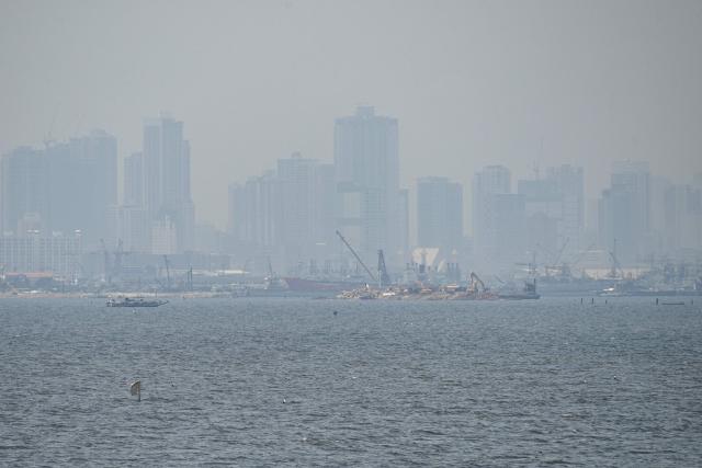 Heavy grey smoke engulfs buildings in Manila City as a burning landfill continues to emit smoke in the nearby Navotas City, as seen from the coast of Obando town, Bulacan province, on April 30, 2026. The fire at Metro Manila's Navotas landfill is largely invisible to the naked eye, combusting as deep as 15 metres (50 feet) below the surface and releasing a toxic brew of methane as well as carbon dioxide. (Photo by Ted ALJIBE / AFP) / To go with "PHILIPPINES-FIRE-WASTE-ENVIRONMENT-POLLUTION, REPORTAGE" BY PAM CASTRO
