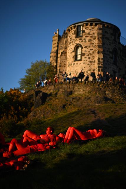 Performers pained red soak up the sun before taking part in the Beltane Fire Festival on Calton Hill, Edinburgh on April 30, 2026. The annual event is inspired by the pre-Christian spring-time festival and is intended to emphasise a connection with the passing of the seasons. (Photo by ANDY BUCHANAN / AFP)
