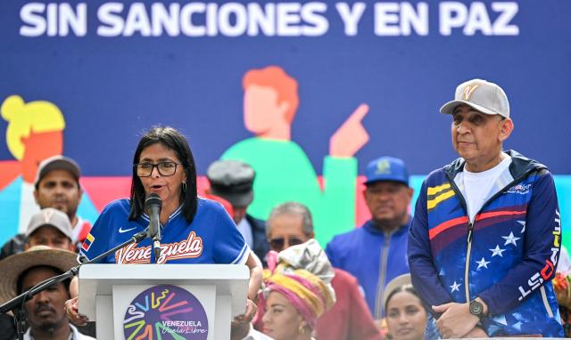 Venezuela's acting president Delcy Rodriguez (L) speaks next to Labor Minister Carlos Castillo during a march calling for the lifting of all US sanctions in Caracas on April 30, 2026. Delcy Rodriguez announced on April 30 a 26% wage increase to the so-called "integral minimum income," raising it from 190 dollars to 240 dollars per month, the first adjustment since Nicolas Maduro's fall. (Photo by Juan BARRETO / AFP)