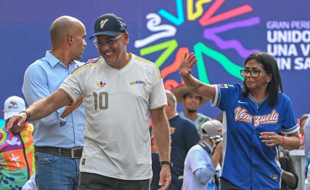 Venezuela's acting president Delcy Rodriguez (R) waves next to National Assembly President Jorge Rodriguez during a march calling for the lifting of all US sanctions in Caracas on April 30, 2026. Delcy Rodriguez announced on April 30 a 26% wage increase to the so-called "integral minimum income," raising it from 190 dollars to 240 dollars per month, the first adjustment since Nicolas Maduro's fall. (Photo by Juan BARRETO / AFP)