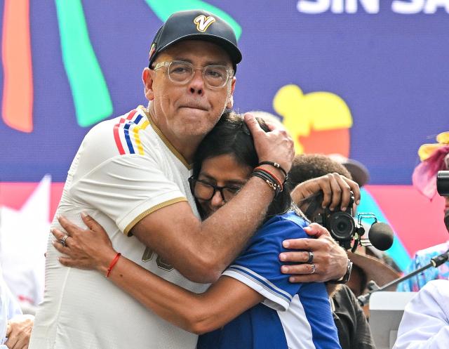 Venezuela's acting president Delcy Rodriguez (R) embraces her brother National Assembly President Jorge Rodriguez, during a march calling for the lifting of all US sanctions in Caracas on April 30, 2026. Delcy Rodriguez announced on April 30 a 26% wage increase to the so-called "integral minimum income," raising it from 190 dollars to 240 dollars per month, the first adjustment since Nicolas Maduro's fall. (Photo by Juan BARRETO / AFP)