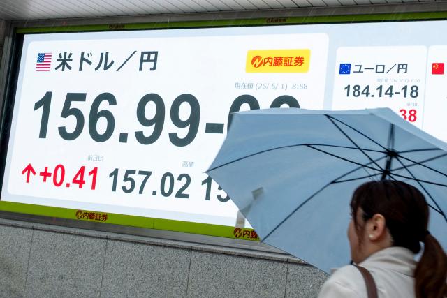A woman walks past an electronic quotation boards displaying the foreign exchange rate of the Japanese yen against the US dollar along a street in Tokyo on May 1, 2026. (Photo by Kazuhiro NOGI / AFP)