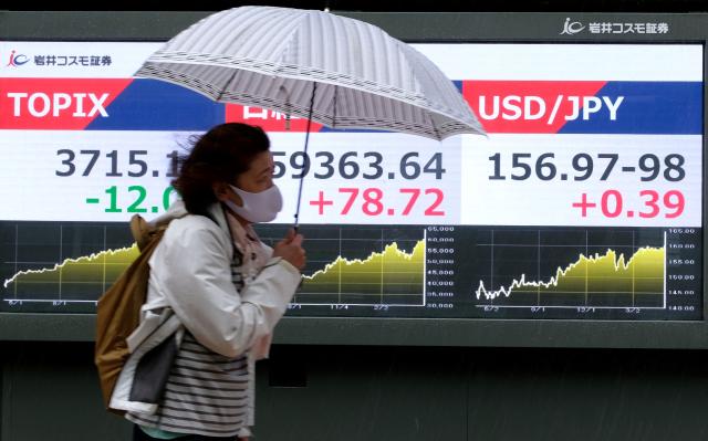 A woman walks past an electronic quotation boards displaying the foreign exchange rate of the Japanese yen against the US dollar (R) along a street in Tokyo on May 1, 2026. (Photo by Kazuhiro NOGI / AFP)