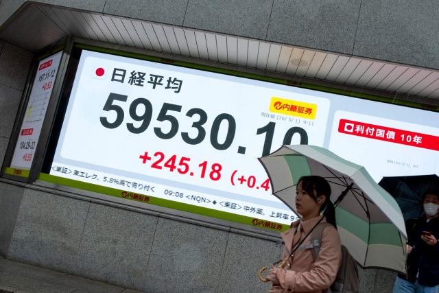 A woman walks past an electronic quotation boards displaying the Nikkei Stock Average on the Tokyo Stock Exchange along a street in Tokyo on May 1, 2026. (Photo by Kazuhiro NOGI / AFP)