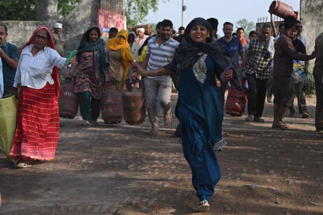 This photograph taken on April 24, 2026 shows people arriving with empty LPG (liquefied petroleum gas) cylinders for refilling, in a village on the outskirts of Uttar Pradesh's Jewar district. Across much of India, an energy crunch caused by the Iran war has prompted long queues for cooking gas cyclinders. However, since the 1980s India has also promoted biogas as a low-cost rural energy source, subsidising more than five million "digester" units that convert farm waste into methane for cooking, and nitrogen-rich slurry for fertiliser. (Photo by Arun SANKAR / AFP)