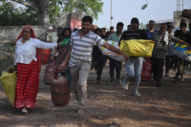 This photograph taken on April 24, 2026 shows people arriving with empty LPG (liquefied petroleum gas) cylinders for refilling, in a village on the outskirts of Uttar Pradesh's Jewar district. Across much of India, an energy crunch caused by the Iran war has prompted long queues for cooking gas cyclinders. However, since the 1980s India has also promoted biogas as a low-cost rural energy source, subsidising more than five million "digester" units that convert farm waste into methane for cooking, and nitrogen-rich slurry for fertiliser. (Photo by Arun SANKAR / AFP)