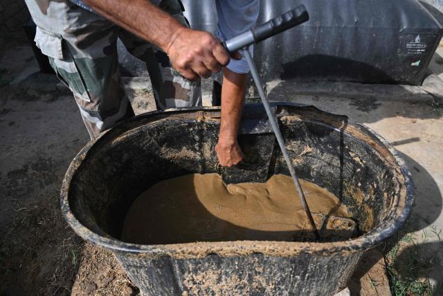 This photograph taken on April 24, 2026 shows a resident pouring cow dung into his biogas plant at a village in Uttar Pradesh's Bulandshahr district. Across much of India, an energy crunch caused by the Iran war has prompted long queues for cooking gas cyclinders. However, since the 1980s India has also promoted biogas as a low-cost rural energy source, subsidising more than five million "digester" units that convert farm waste into methane for cooking, and nitrogen-rich slurry for fertiliser. (Photo by Arun SANKAR / AFP)