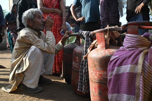 This photograph taken on April 24, 2026 shows people waiting with empty LPG (liquefied petroleum gas) cylinders for refilling, in a village on the outskirts of Uttar Pradesh's Jewar district. Across much of India, an energy crunch caused by the Iran war has prompted long queues for cooking gas cyclinders. However, since the 1980s India has also promoted biogas as a low-cost rural energy source, subsidising more than five million "digester" units that convert farm waste into methane for cooking, and nitrogen-rich slurry for fertiliser. (Photo by Arun SANKAR / AFP)