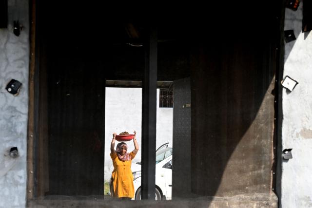 This photograph taken on April 24, 2026 shows a villager carrying cow dung from her cattle stable to a biogas plant at her residence in Uttar Pradesh's Bulandshahr district. Across much of India, an energy crunch caused by the Iran war has prompted long queues for cooking gas cyclinders. However, since the 1980s India has also promoted biogas as a low-cost rural energy source, subsidising more than five million "digester" units that convert farm waste into methane for cooking, and nitrogen-rich slurry for fertiliser. (Photo by Arun SANKAR / AFP)
