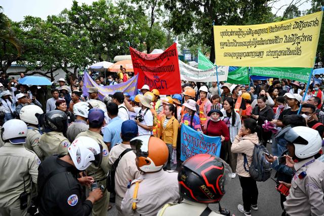 Security personnel (L) block a street as Cambodian workers march toward to the British embassy during a protest to mark the International Labour Day in Phnom Penh on May 1, 2026. (Photo by TANG CHHIN Sothy / AFP)