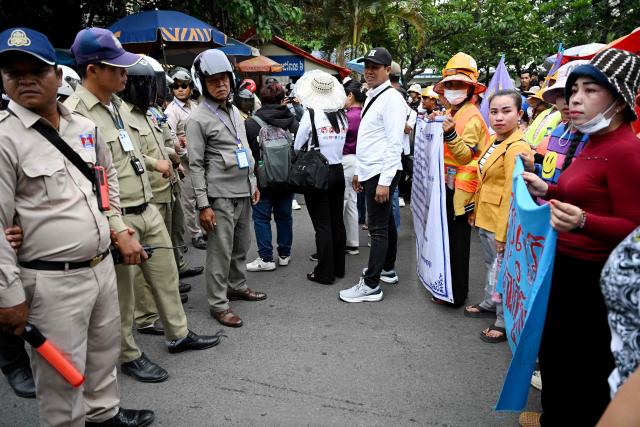 Security personnel (L) block a street as Cambodian workers march toward to the British embassy during a protest to mark the International Labour Day in Phnom Penh on May 1, 2026. (Photo by TANG CHHIN Sothy / AFP)