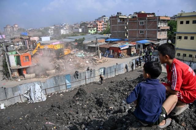 TOPSHOT - Boys watch as heavy construction equipment is used to demolish squatter settlements near the Bagmati River in Kathmandu on May 1, 2026. Nepali authorities has been demolishing informal settlements to thousands of people along river banks of the capital, despite criticism from rights groups. (Photo by PRAKASH MATHEMA / AFP)