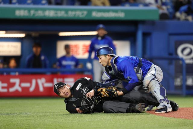 This picture taken on April 16, 2026 shows Japanese professional baseball umpire Takuto Kawakami (L) being struck and knocked down by a bat that slipped from the hands of Jose Osuna of the Yakult Swallows at the Meiji Jingu Stadium in Tokyo. (Photo by JIJI PRESS / AFP) / Japan OUT