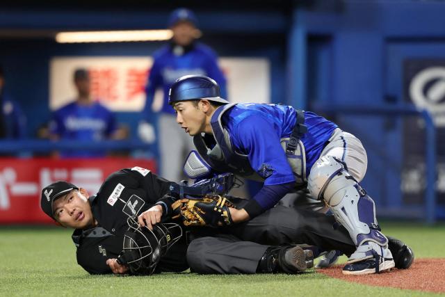 This picture taken on April 16, 2026 shows Japanese professional baseball umpire Takuto Kawakami (L) being struck and knocked down by a bat that slipped from the hands of Jose Osuna of the Yakult Swallows at the Meiji Jingu Stadium in Tokyo. (Photo by JIJI PRESS / AFP) / Japan OUT