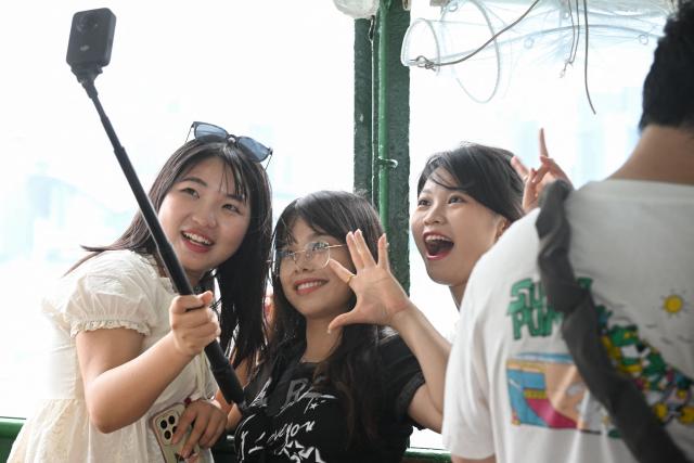 Tourists take photos on the Star Ferry during China's Labour Day golden week holiday in Hong Kong on May 1, 2026. (Photo by Peter PARKS / AFP)