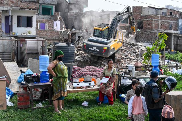 TOPSHOT - People watch as heavy construction equipment is used to demolish squatter settlements near the Bagmati River in Kathmandu on May 1, 2026. Nepali authorities has been demolishing informal settlements to thousands of people along river banks of the capital, despite criticism from rights groups. (Photo by PRAKASH MATHEMA / AFP)