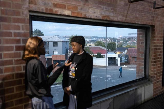 A man walks on a street next to a mural depicting a middle finger as attendees talk at the launch of “Finishing What Was Started”, an event reflecting on the legacy of the June 1976 generation and a call to action for today’s youth, at the Hector Pieterson Museum in Soweto on April 30, 2026. (Photo by EMMANUEL CROSET / AFP)