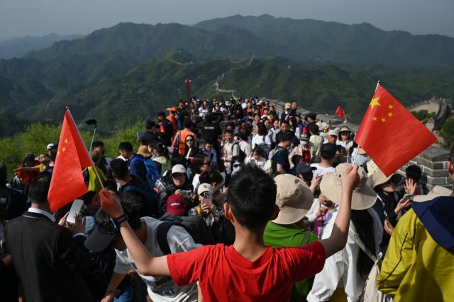 A boy poses for photos with Chinese flags on the Great Wall of China at Badaling, north of Beijing, on May 1, 2026, on the first day of a five-day national May Day holiday. (Photo by GREG BAKER / AFP)