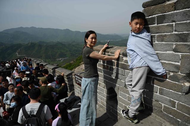 A woman and child pose for photos on the Great Wall of China at Badaling, north of Beijing, on May 1, 2026, on the first day of a five-day national May Day holiday. (Photo by GREG BAKER / AFP)