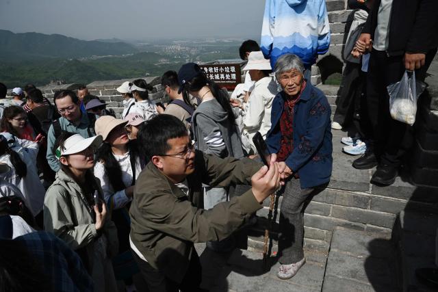 A woman rests as others take photos on the Great Wall of China at Badaling, north of Beijing, on May 1, 2026, on the first day of a five-day national May Day holiday. (Photo by GREG BAKER / AFP)