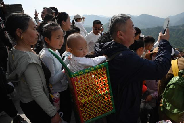 A man carries a child in a basket as he takes photos on the Great Wall of China at Badaling, north of Beijing, on May 1, 2026, on the first day of a five-day national May Day holiday. (Photo by GREG BAKER / AFP)