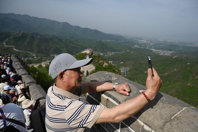 A man takes photos on the Great Wall of China at Badaling, north of Beijing, on May 1, 2026, on the first day of a five-day national May Day holiday. (Photo by GREG BAKER / AFP)