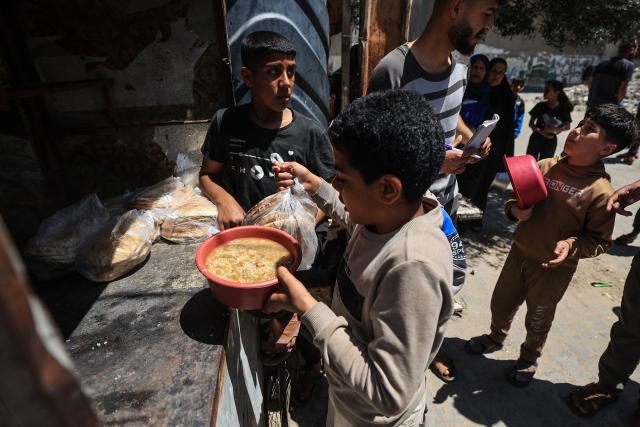 A displaced Palestinian boy, whose home was destroyed by the Israeli military, collects food from a charity kitchen in the Bureij refugee camp, in the central Gaza Strip on May 1, 2026. The war on the Gaza Strip was sparked following the militant Palestinian group Hamas's October 7, 2023 attack on Israel, which resulted in the deaths of 1,221 people. Israel's retaliatory assault on Gaza has killed at least 72,600 people, according to figures from the health ministry that the UN considers reliable. with th  majority of Gaza's 2.4 million people being displaced. (Photo by Eyad Baba / AFP)
