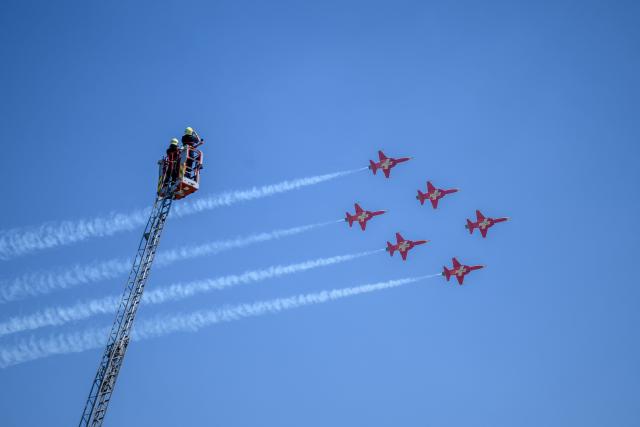 Firefighters on a large ladder photograph the flypast performed by the Swiss Air Force's aerobatic team "The Patrouille Suisse", during the third stage of the Tour of Romandie UCI cycling World tour, a 176.6 km loop from Orbe to Orbe, in Orbe, Switzerland, on May, 1, 2026. (Photo by Fabrice COFFRINI / AFP)