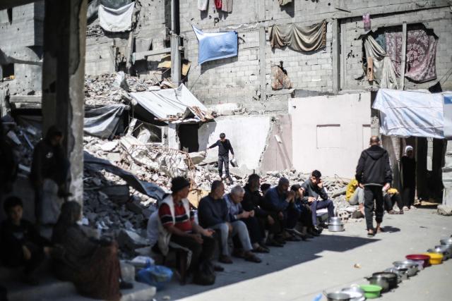 Displaced Palestinians sit with their empty containers on the rubble of buildings destroyed by the Israeli military, as they wait to collect food from a charity kitchen in the Bureij refugee camp in the central Gaza Strip on May 1, 2026. The war on the Gaza Strip was sparked following the militant Palestinian group Hamas's October 7, 2023 attack on Israel, which resulted in the deaths of 1,221 people. Israel's retaliatory assault on Gaza has killed at least 72,600 people, according to figures from the health ministry that the UN considers reliable. with th  majority of Gaza's 2.4 million people being displaced. (Photo by Eyad Baba / AFP)