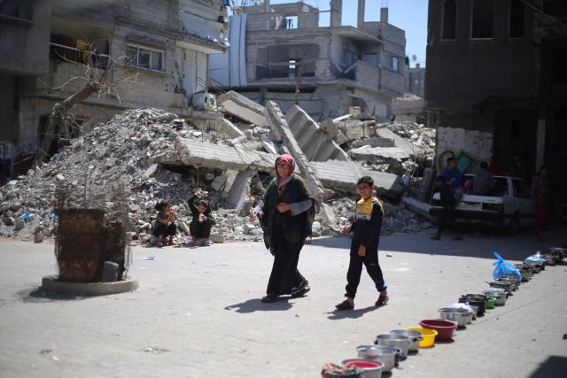 A displaced Palestinian woman and child walk past a row of empty food containers placed near the rubble of buildings destroyed by the Israeli military, as families wait to collect food from a charity kitchen in the Bureij refugee camp, in the central Gaza Strip on May 1, 2026. The war on the Gaza Strip was sparked following the militant Palestinian group Hamas's October 7, 2023 attack on Israel, which resulted in the deaths of 1,221 people. Israel's retaliatory assault on Gaza has killed at least 72,600 people, according to figures from the health ministry that the UN considers reliable. with th  majority of Gaza's 2.4 million people being displaced. (Photo by Eyad Baba / AFP)