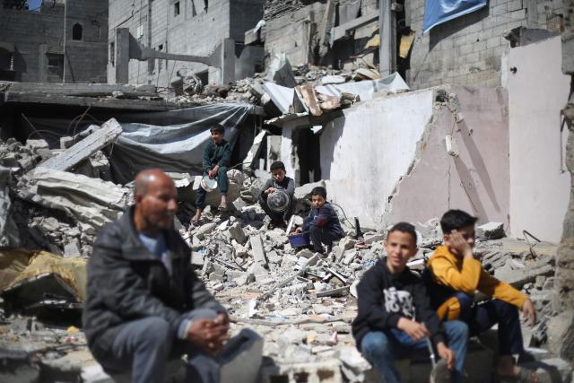 Displaced Palestinians sit with their empty containers amid the rubble of buildings destroyed by the Israeli military, as they wait to collect food from a charity kitchen in the Bureij refugee camp in the central Gaza Strip on May 1, 2026. The war on the Gaza Strip was sparked following the militant Palestinian group Hamas's October 7, 2023 attack on Israel, which resulted in the deaths of 1,221 people. Israel's retaliatory assault on Gaza has killed at least 72,600 people, according to figures from the health ministry that the UN considers reliable. with th  majority of Gaza's 2.4 million people being displaced. (Photo by Eyad Baba / AFP)
