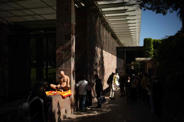 A visitor in swimsuit reads a book at the main entrance of the Beyeler Foundation during the experience called "bathers' day" ("journée des baigneurs et des baigneuses") inspired by Italian artist Maurizio Cattelan, on the occasion of the exhibition "Cezanne" of the French painter Paul Cezanne at the Beyeler Foundation in Riehen, northern Switzerland on May 1, 2026. (Photo by SEBASTIEN BOZON / AFP)
