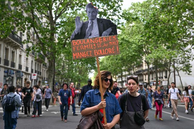A woman holds a placard reading "Bakeries closed on May 1? Let them eat Bollore" during a May Day rally marking International Workers' Day in Paris, on May 1, 2026. (Photo by Julie SEBADELHA / AFP)