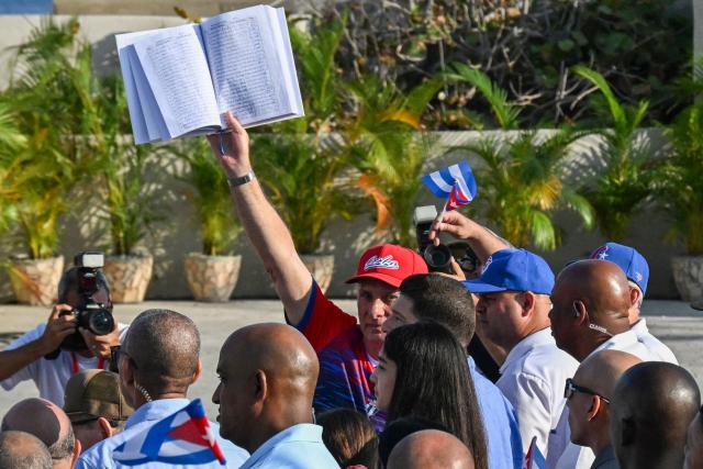 Cuba's President Miguel Diaz-Canel raises a book signed by Cubans as a pledge to the homeland and in defense of national sovereignty, against the US blockade and for peace, during May Day celebrations marking International Workers’ Day in Havana on May 1, 2026. (Photo by YAMIL LAGE / AFP)
