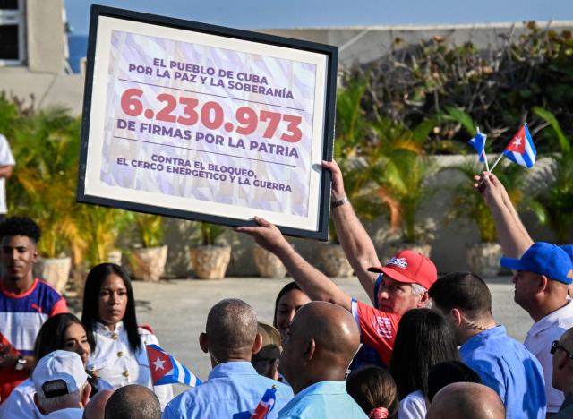 Cuba's President Miguel Diaz-Canel raises a board showing the number of Cuban signatures pledging commitment to the homeland and defense of national sovereignty, against the US blockade and in favor of peace, during May Day celebrations marking International Workers' Day in Havana on May 1, 2026. (Photo by YAMIL LAGE / AFP)