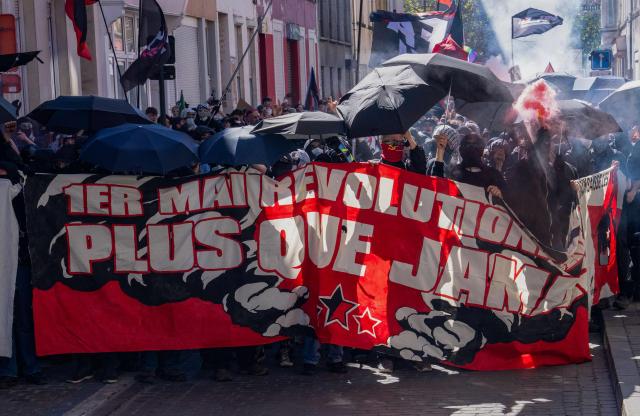 Demonstrators with umbrellas hold a banner reading "1st of May, more revolutionary than ever" during the May Day (Labor Day) rally, marking International Workers' Day, in Brussels on May 1, 2026. (Photo by Marius BURGELMANS / Belga / AFP) / Belgium OUT