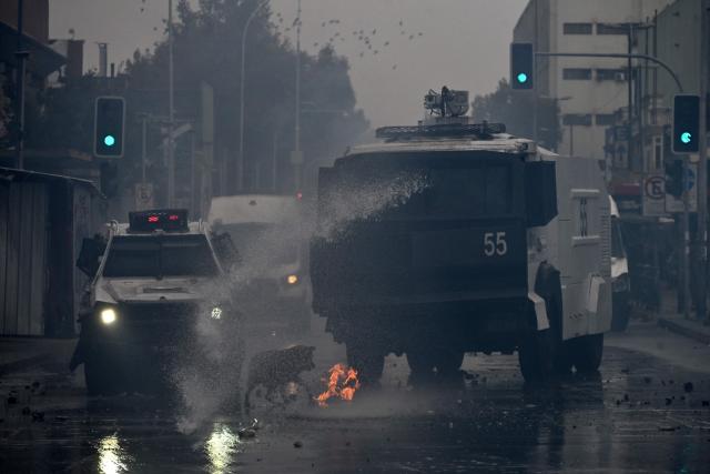 A riot police water cannon truck sprays water at demonstrators during a march organized by unions and social organizations on May Day, marking International Workers Day, in Santiago, on May 1, 2026. (Photo by RODRIGO ARANGUA / AFP)