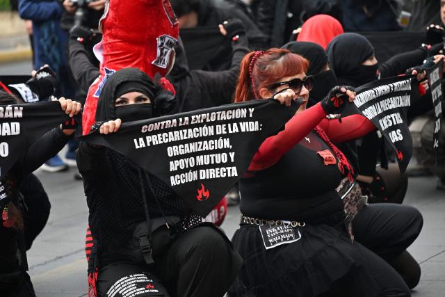 Workers hold scarves reading "Against exploitation and the precarization of life: organization, mutual support and direct action" during a march organized by unions and social organizations on May Day, marking International Workers Day, in Santiago, on May 1, 2026. (Photo by RODRIGO ARANGUA / AFP)