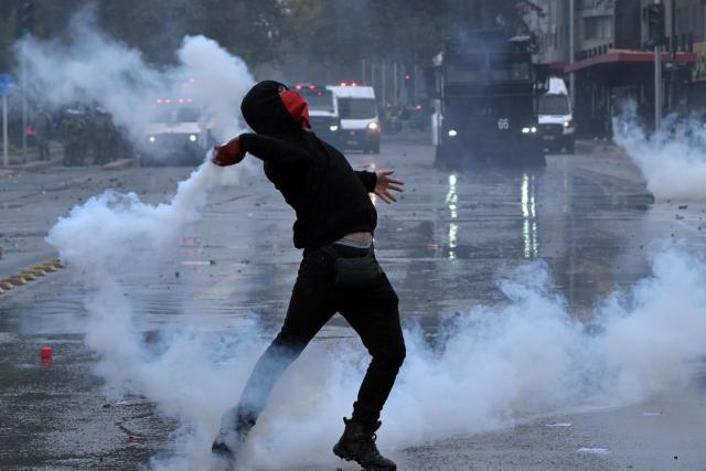 A demonstrator throws back a tear gas canister at riot police during a march organized by unions and social organizations on May Day, marking International Workers Day, in Santiago, on May 1, 2026. (Photo by Rodrigo ARANGUA / AFP)
